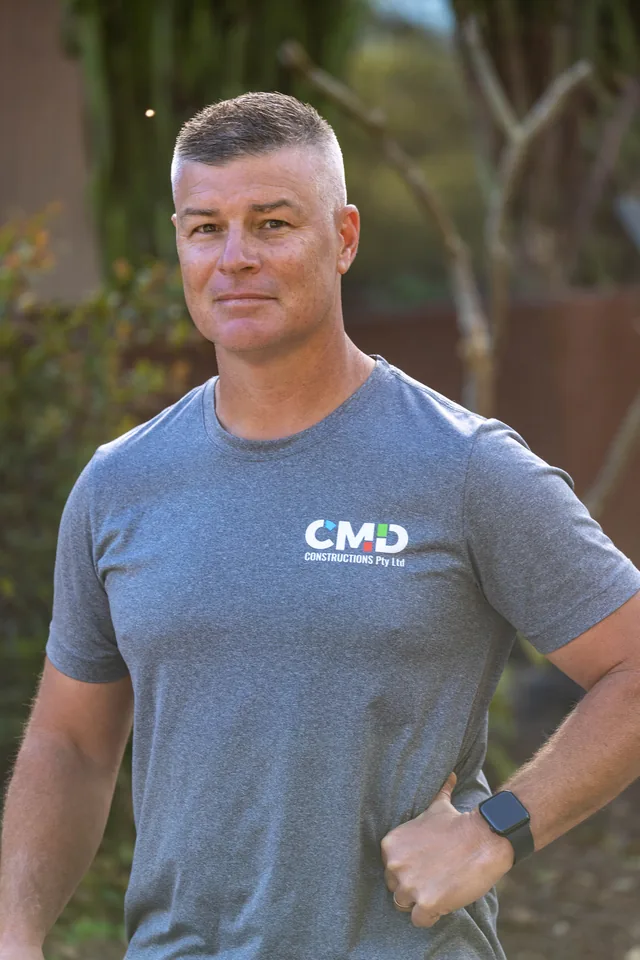 Cade Davidson on site, in a CMD Constructions shirt with one hand on his hip, looking to camera.
