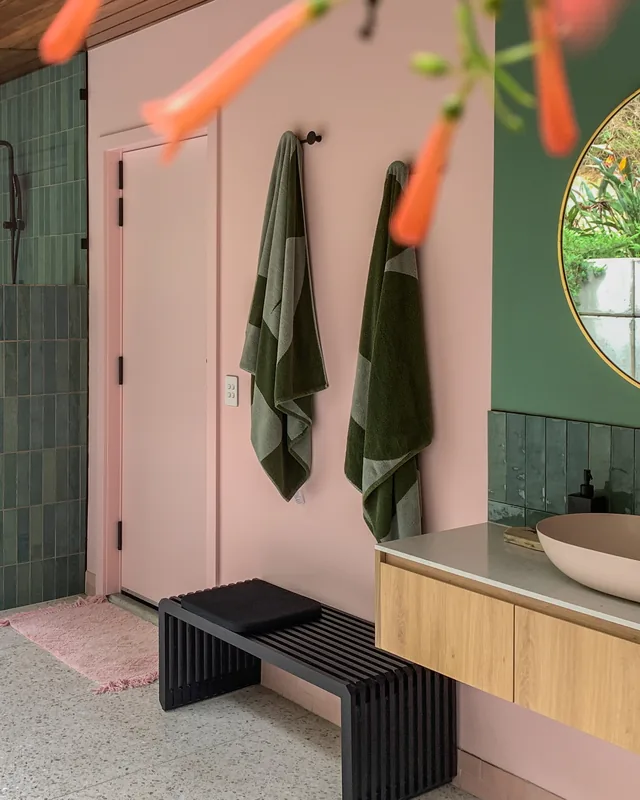The bathroom from the other end, green tile against pink, a timber vanity and a terrazzo floor.
