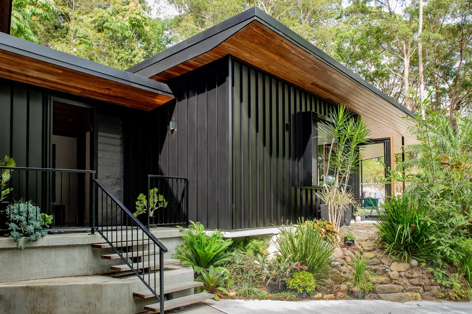 The east end of the house, black standing-seam cladding rising to a raking timber-lined roof over a steel stair.