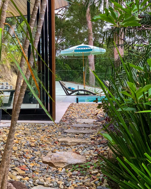 A stepping-stone path through river pebbles and planting, running alongside the black cladding down towards the pool.