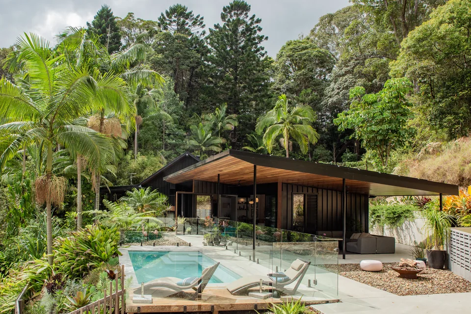 The house and pool seen from higher on the site, framed by palms and rainforest.