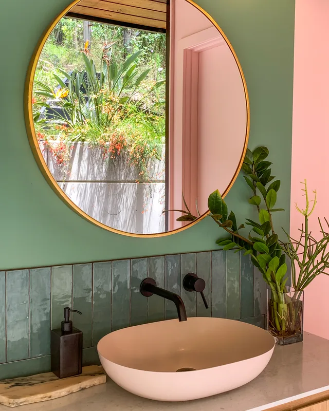 A round brass-rimmed mirror above a pink stone basin with a wall-mounted black mixer.