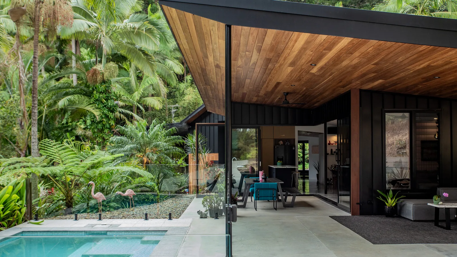 The west face of the house, its timber-lined eave carried out over a pool terrace, with glass doors open to the living room.